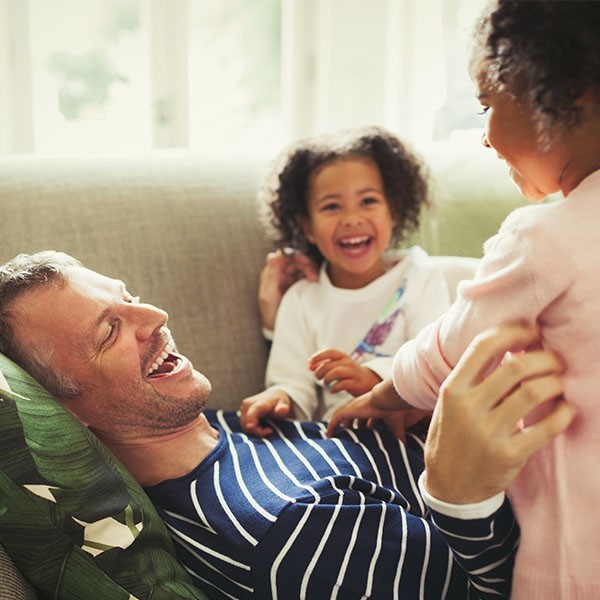 Man laughing on couch with two young girls