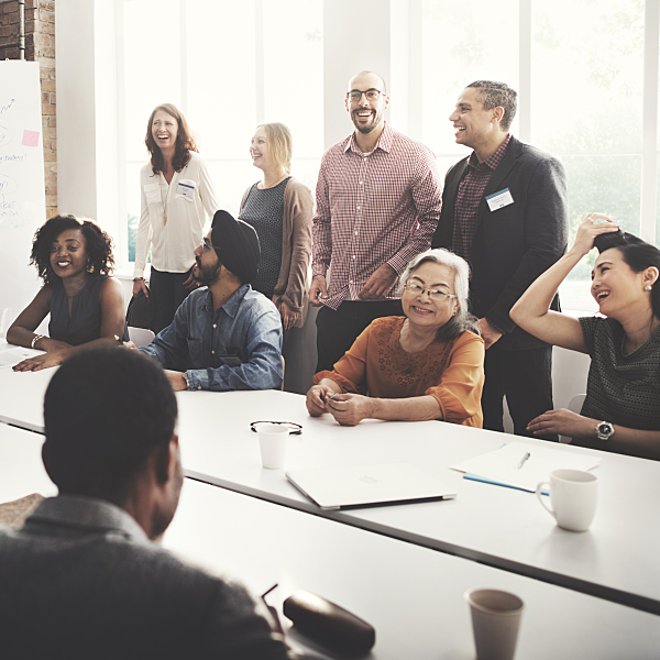 A diverse group of employees of a variety of ages, genders, and races laughing in a conference room during a presentation