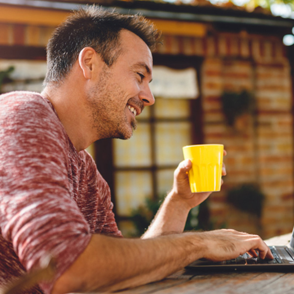 A man with a cup of coffee working on a laptop outside