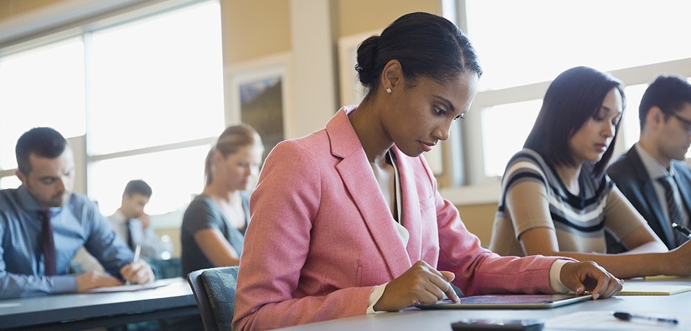 Young professional woman uses her tablet while seated at a table of people