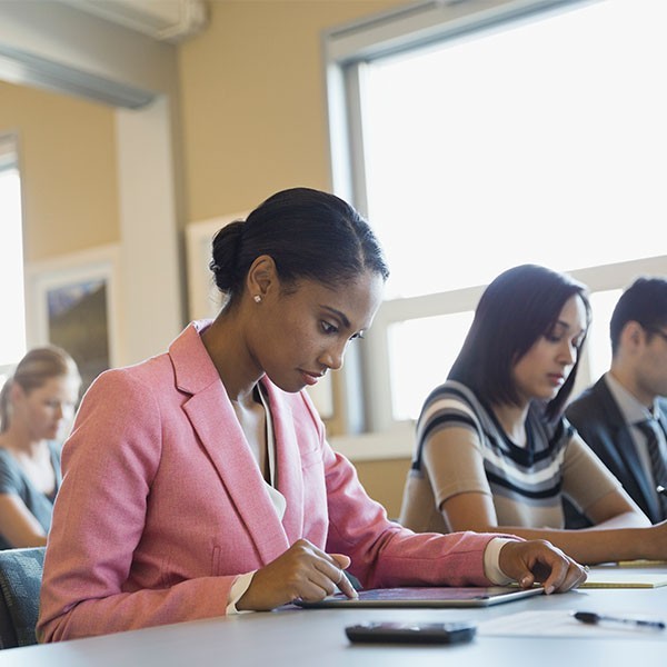 Young professional woman uses her tablet while seated at a table of people
