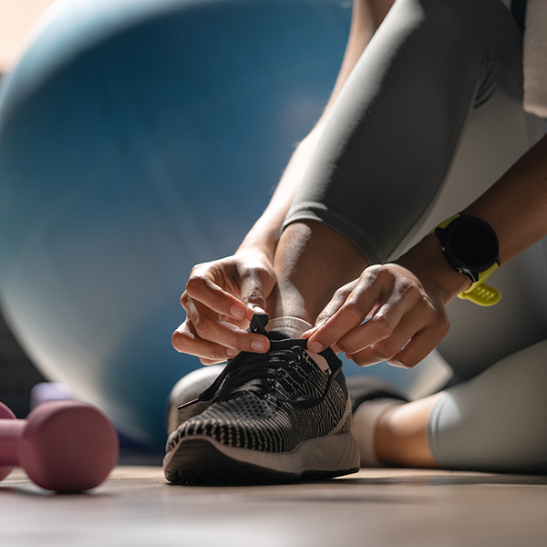 A person of color lacing an athletic show in a gym