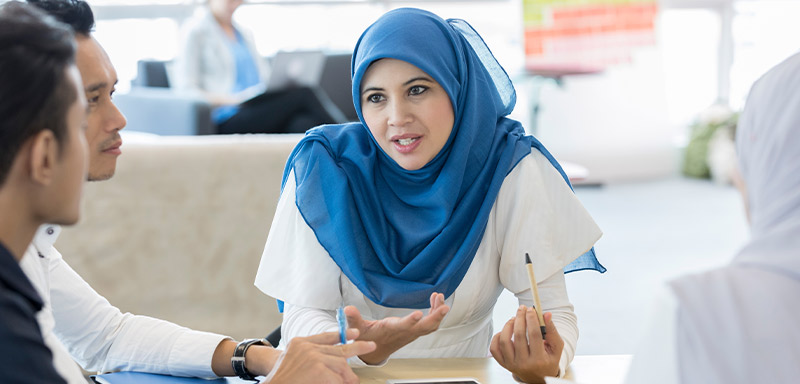 A woman wearing a hijab leading a business meeting