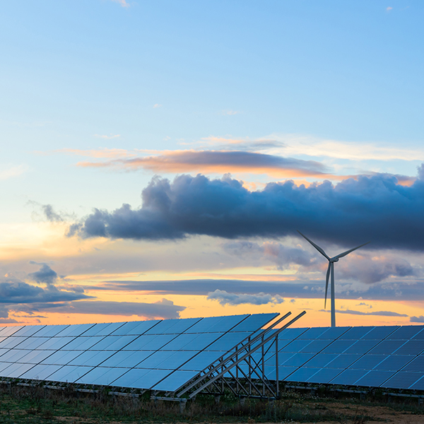 Solar panels and a wind turbine in the foreground of a sunset scene