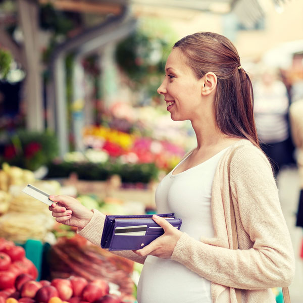 Young pregnant woman uses a credit card to purchase produce at a market