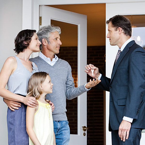 Family standing in front of house, realtor hands over keys