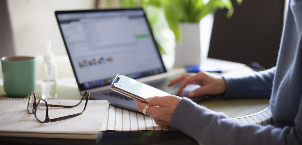 woman using laptop and holding mobile phone in hand
