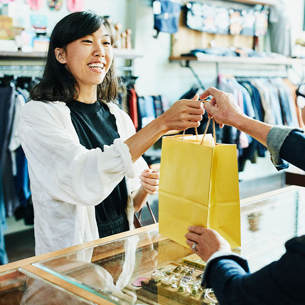 woman handing shopping bag to customer at retail store